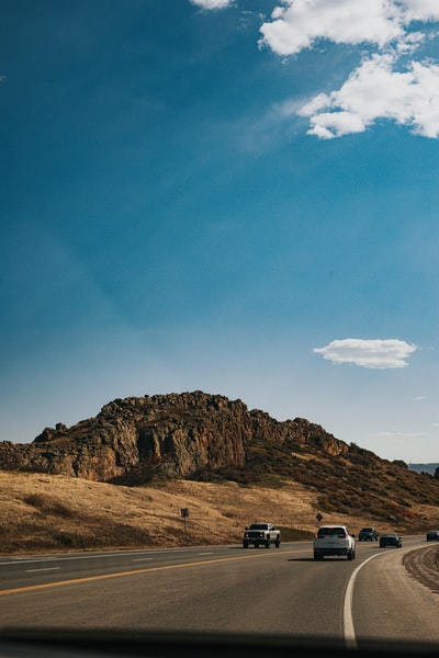 Under the blue sky in the daytime brown hill near the cars on the road
